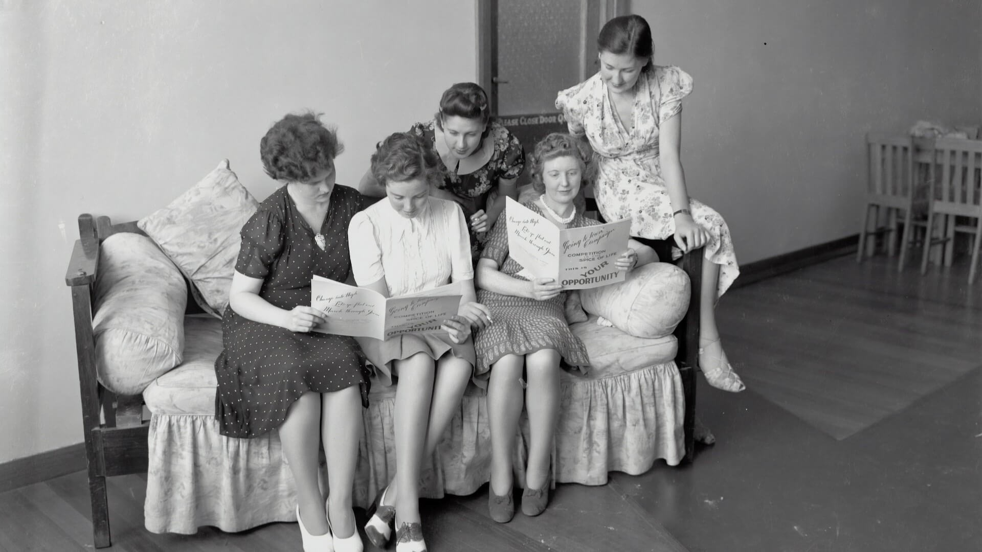 An old photo of a group of five women reading a vintage magazine